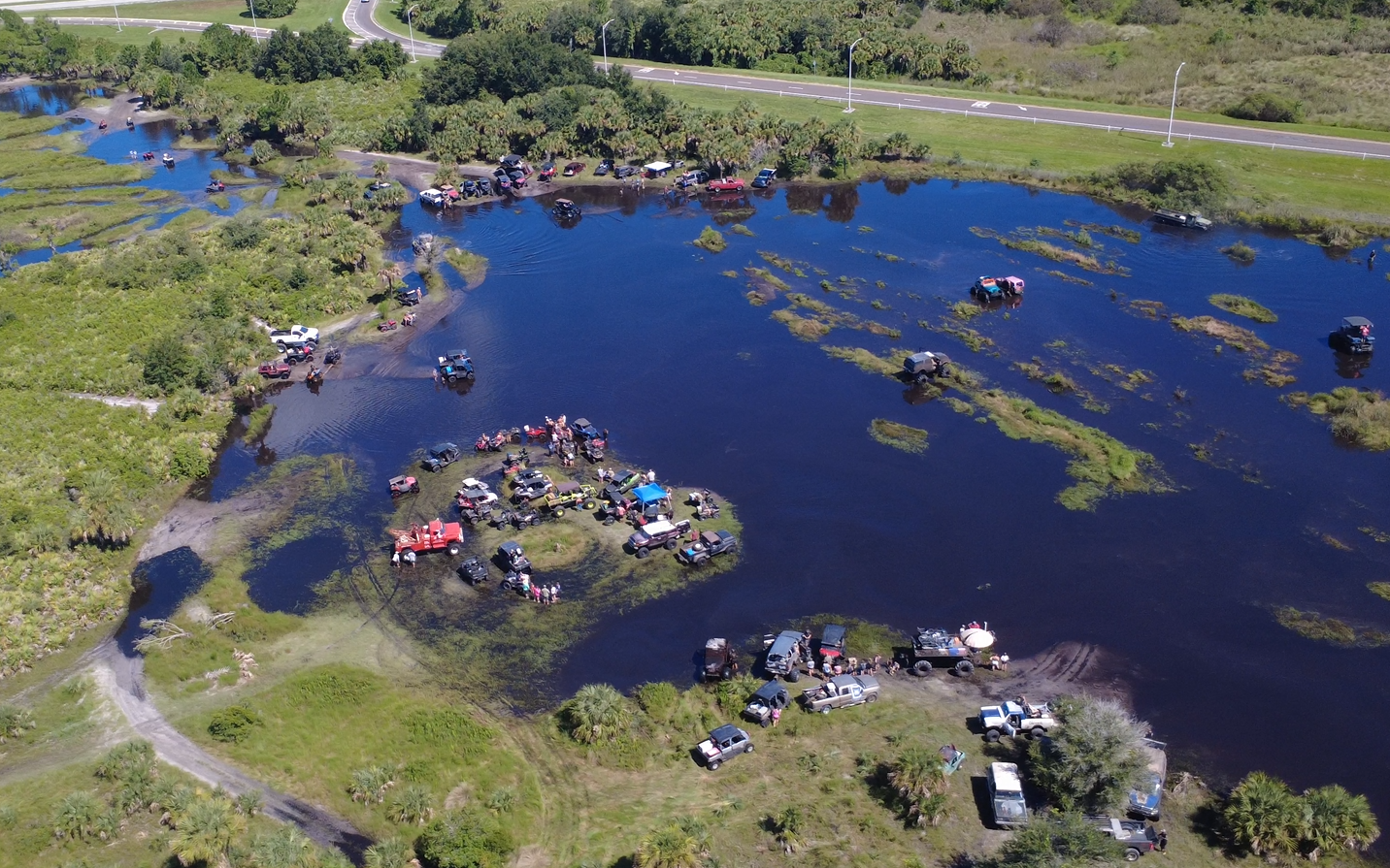 Aerial view of off-road vehicles and spectators around a large water crossing